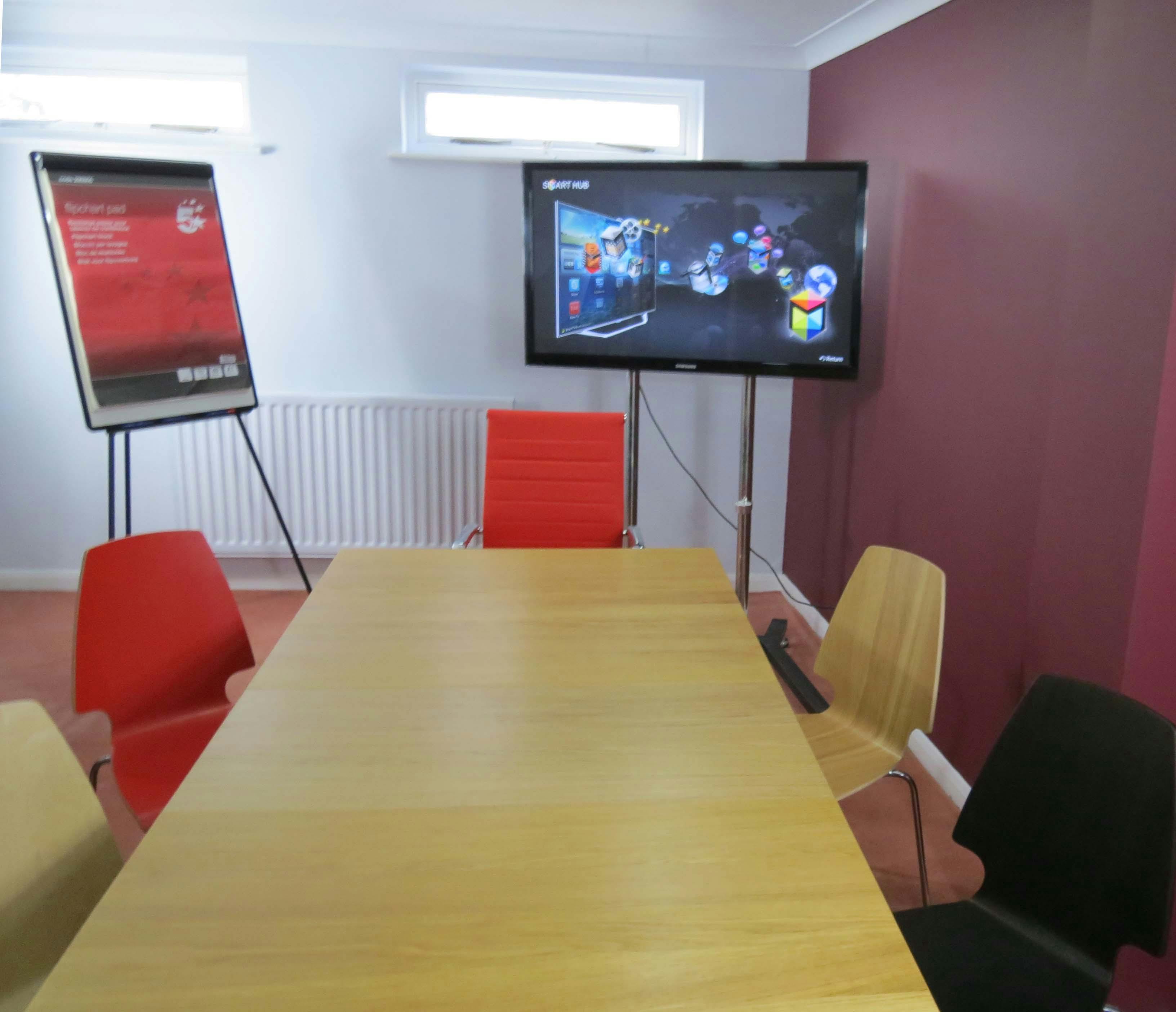 Modern meeting room with wooden table, colorful chairs for collaborative events.